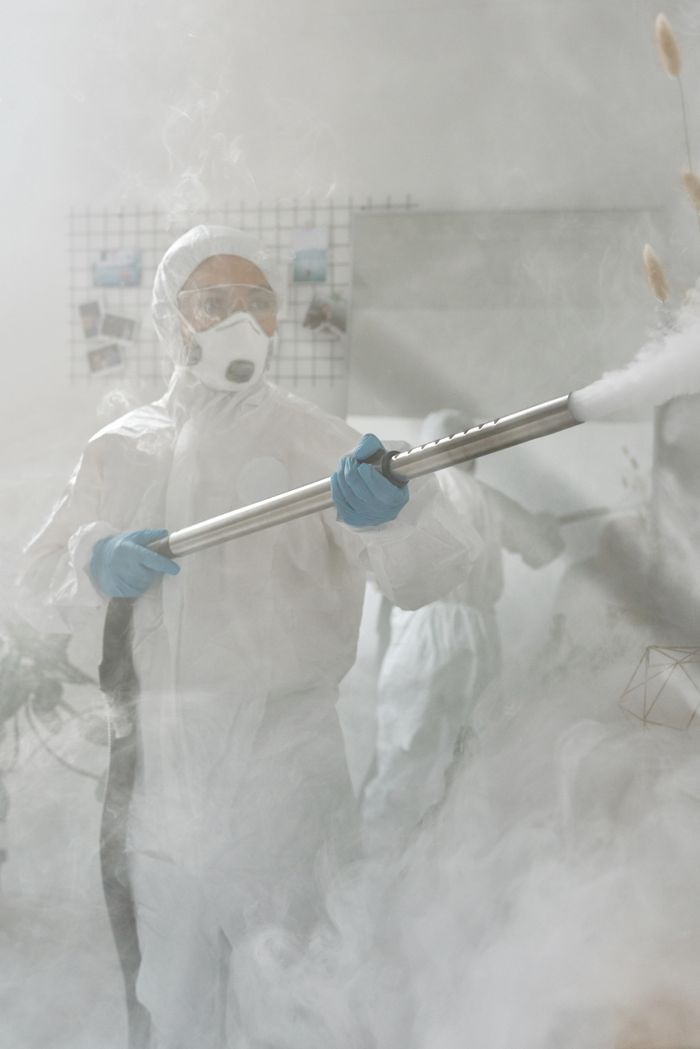Une personne portant un équipement de protection complet pulvérise une pièce afin d’assurer une stérilisation contre les virus.